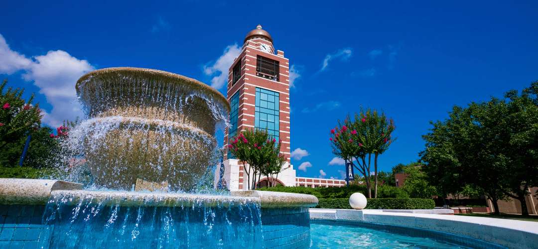 The UAFS Bell Tower overlooking the vibrant campus green and gardens, with the Baldor Building in the background—an inviting view of campus life waiting to be experienced on your tour.